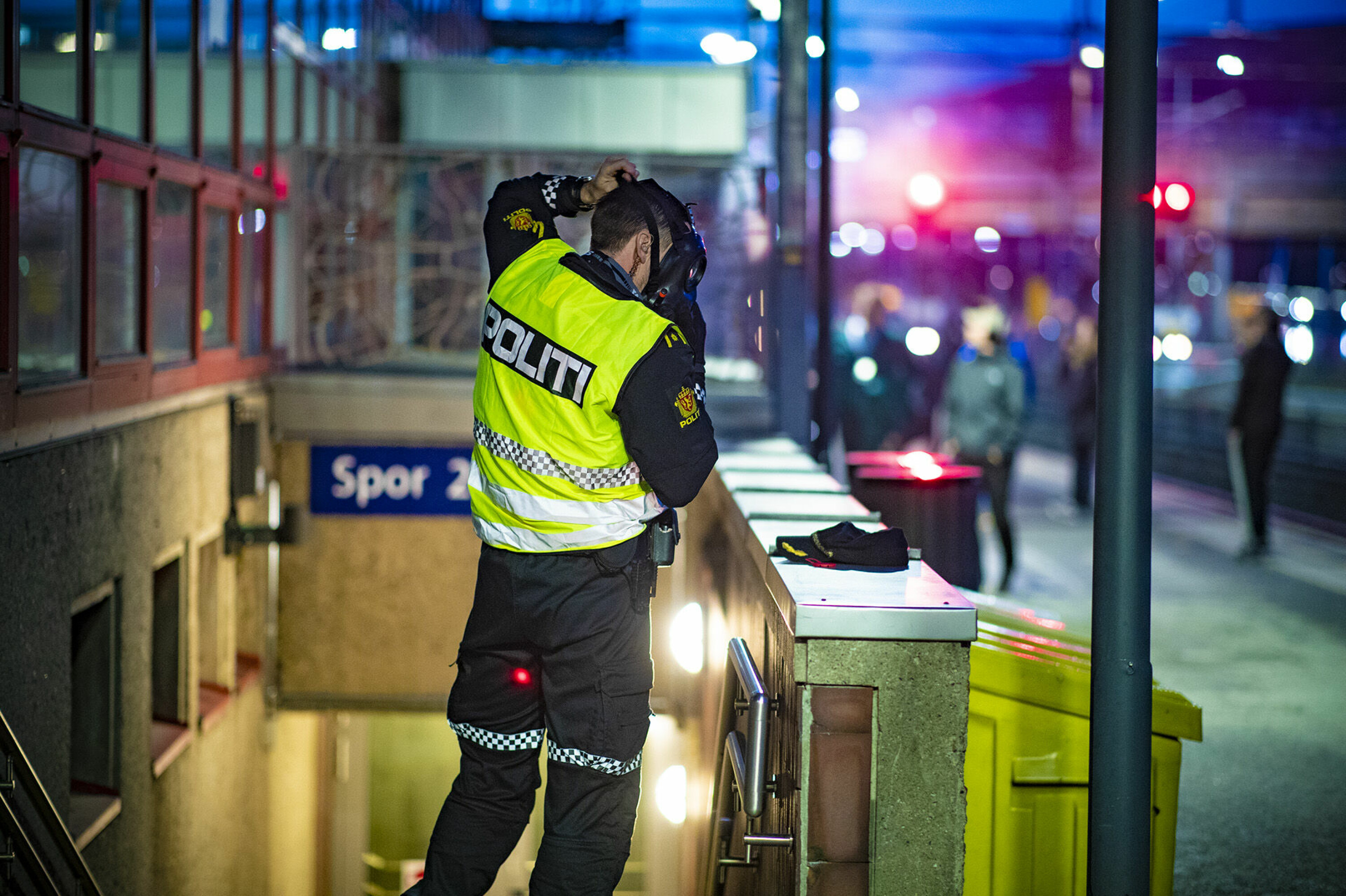 PÅ MED GASSMASKE: En politimann som holder vakt ved en av inngangene tar på seg gassmaske. Røyken veltet ut av alle innganger fra stasjonen.