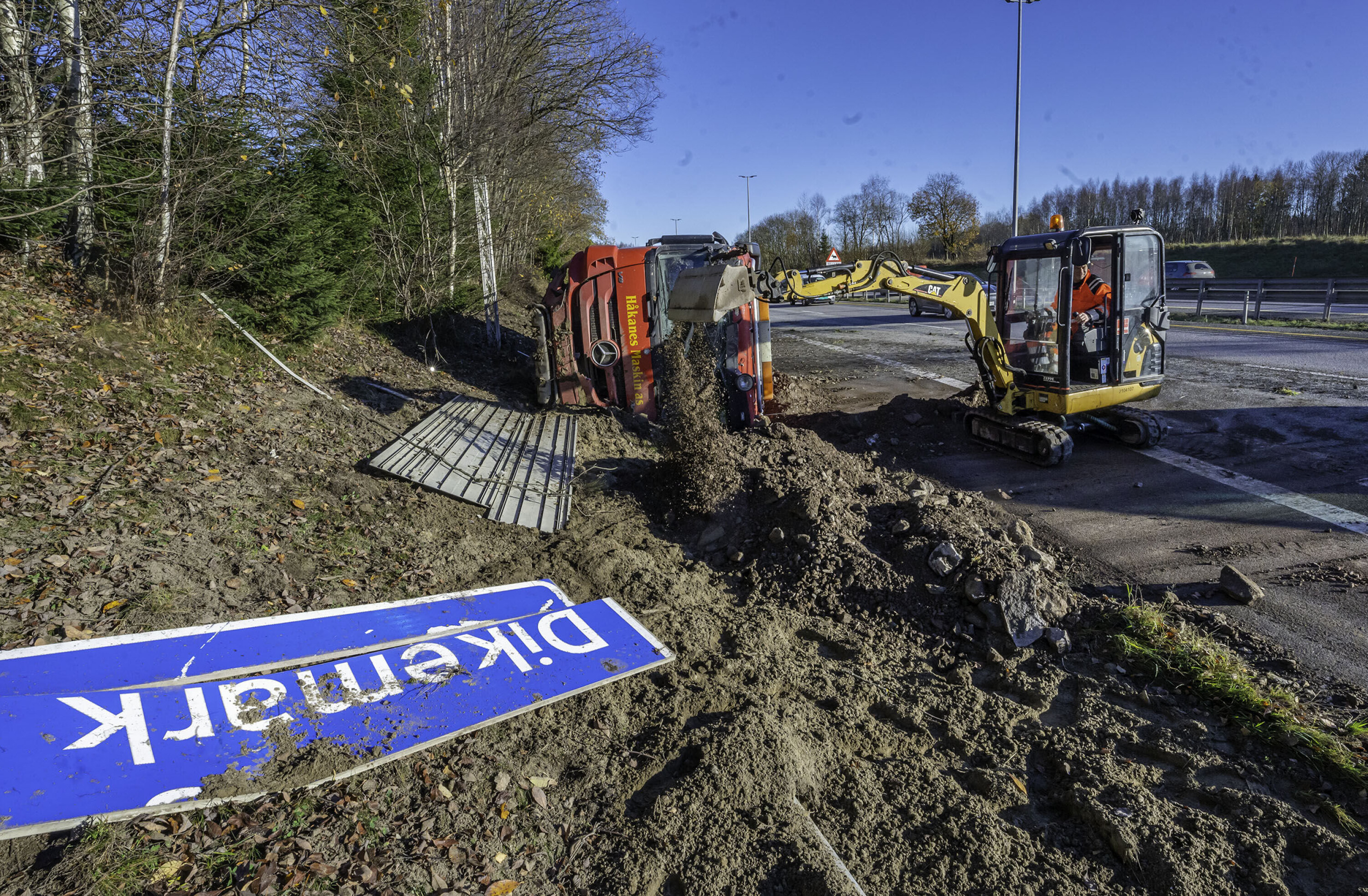 OPPRYDNING: Lastebilen var lastet med jord, sand og stein, og en gravemaskin ankom stedet etter kort tid for å fjerne lasten mens trafikken passerte i ett felt. Veiskiltet til Dikemark fikk også hard medfart i utforkjøringen.