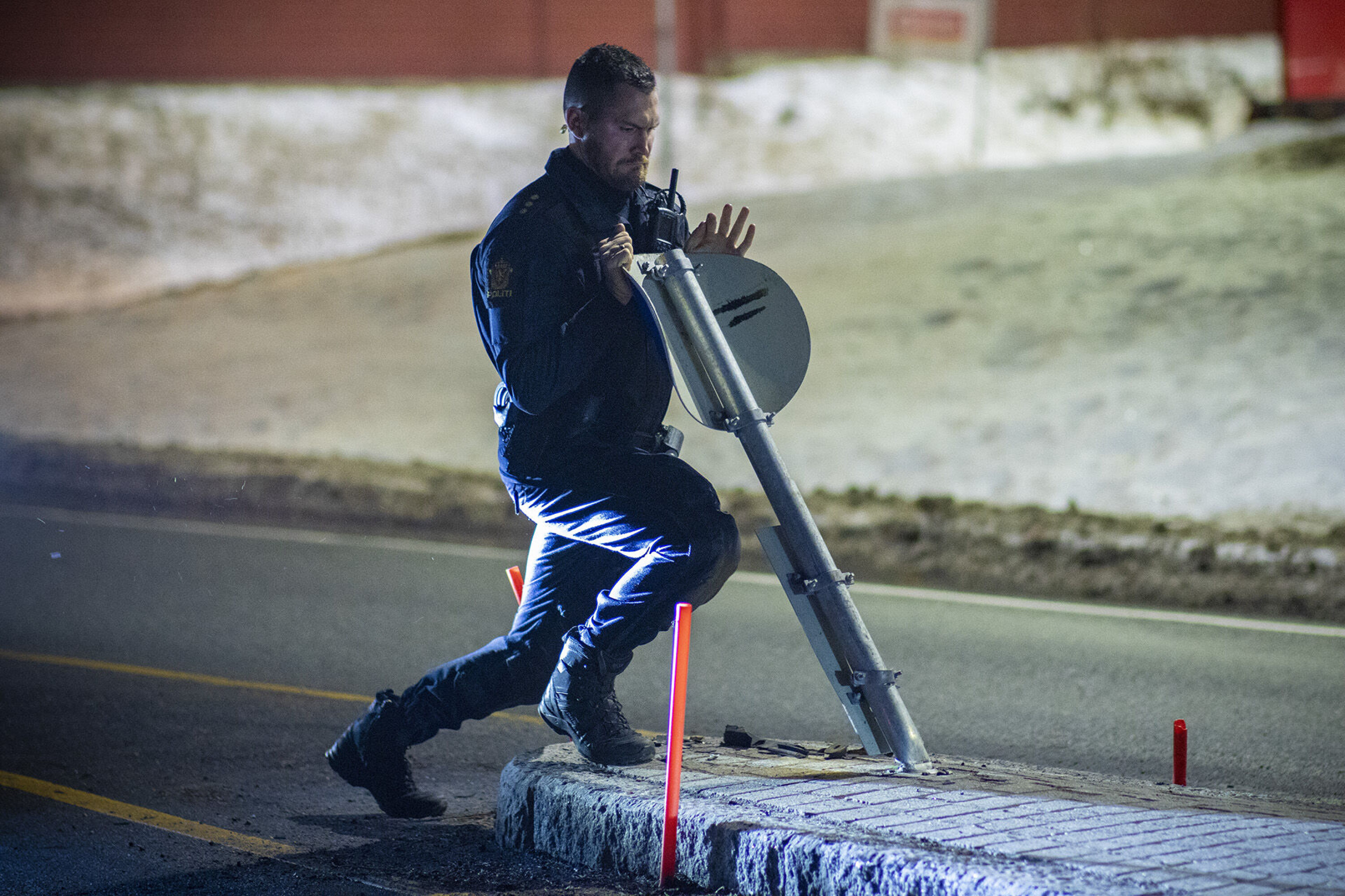 SKADER: Et skilt og noen brøytepinner fikk hard medfart da bilen kjørte over trafikkøya. Her forsøker politimannen med delvis hell å rette opp skiltet igjen.
