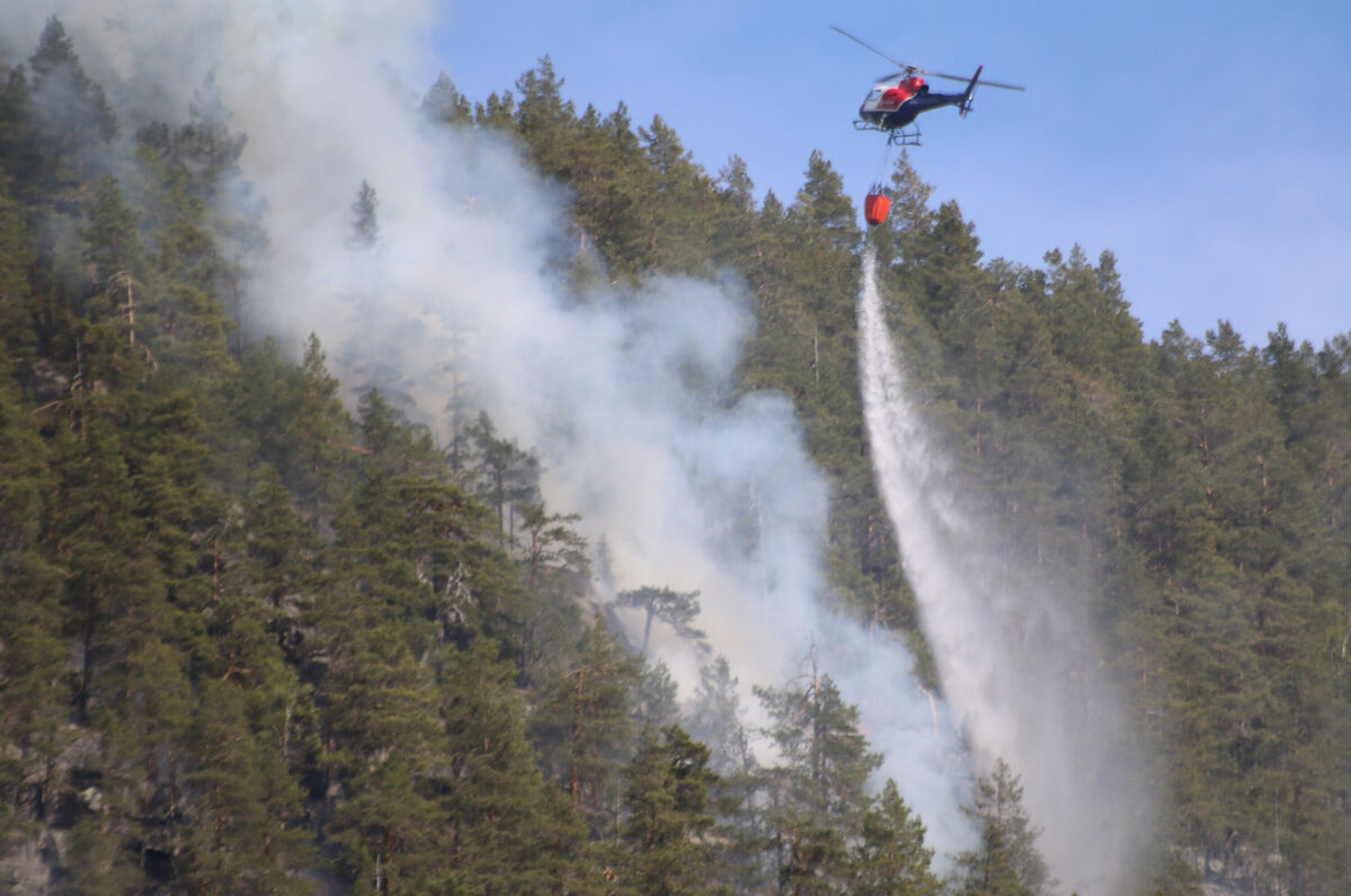 ULENDT TERRENG: Her er skogbrannhelikopteret i aksjon, mandag har bakkemannskapene fått bistand fra to helikoptre som har gjort god nytte for seg.
