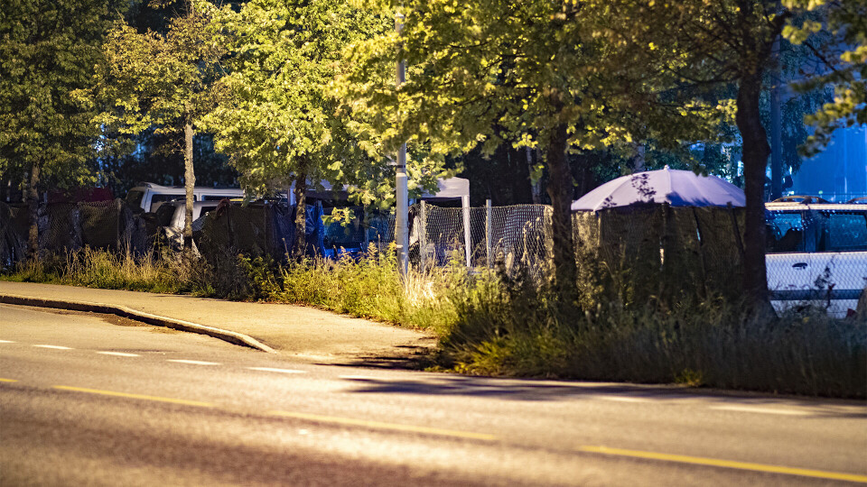 CAMPING: Her ved bussholdeplassen ved Coop Extra på Rundtom har romfolket fått sin egen campingplass, og dekket til gjerdet langs veien med presenninger.GRILLING OG SØPPEL: Romfolket sover i bilene på stedet, mens de utenfor har rigget til en provosorisk campingpass med grill, her sett fra Tollbukaia.