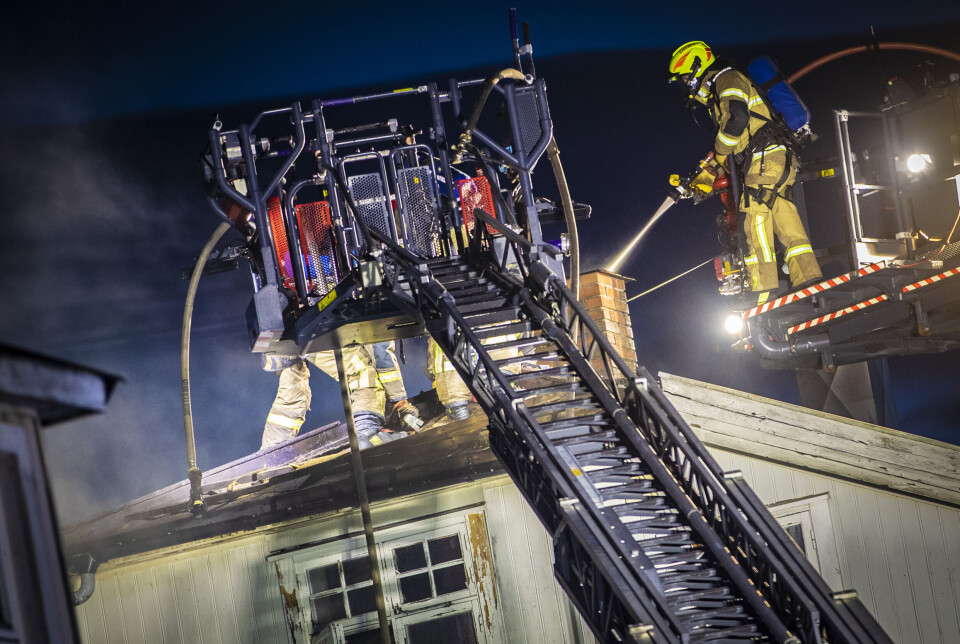 SLUKKER FORTSATT: Brannvesenet jobber for å få kontroll på flammene i den store, gamle bygården nærmest sjøboden.