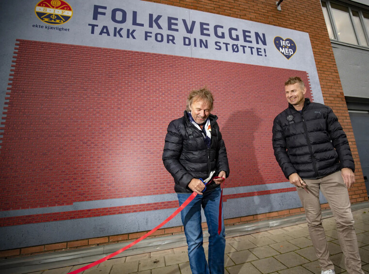 FRA KRONERULLING TIL HODERULLING: Den såkalte Folkeveggen som ble reist på Marienlyst stadion i 2020 genererte 2,5 millioner kroner fra supportere og vanlige folk for klubben i en vanskelig periode, her avduket ved to av klubbens bautaer gjennom mange år - «Mr. Strømsgodset», markedssjef Rune Marthinsen og sportssjef Jostein Flo. Siden har klubben kvittet seg med fire trenere.